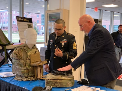 Army soldier talks with a man in a business suit at a table.
