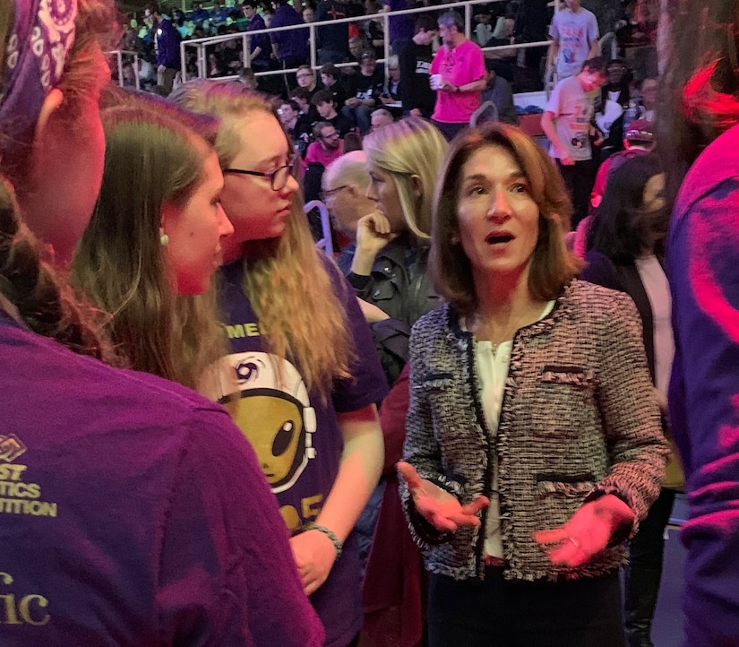 Woman in business suit talks with students.