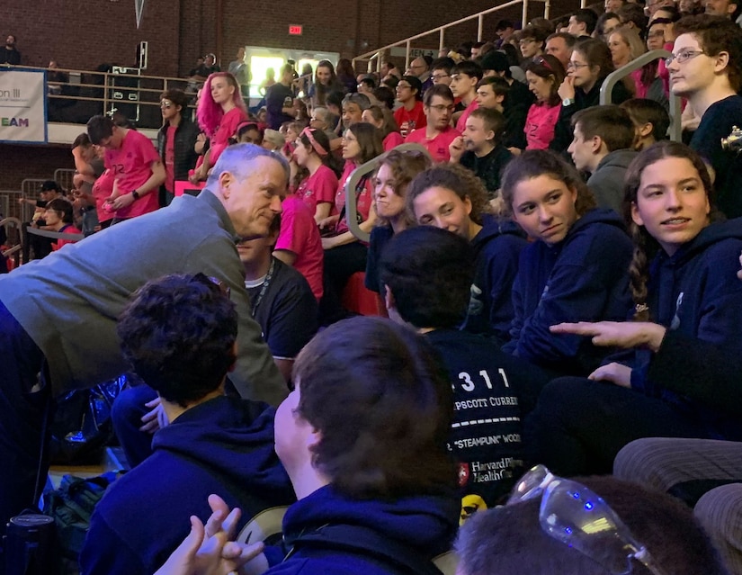 adult governor of Massachusetts talks with high school students on gym bleachers.