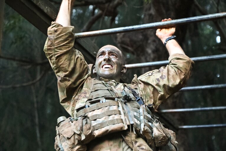 A soldier scales monkey bars.