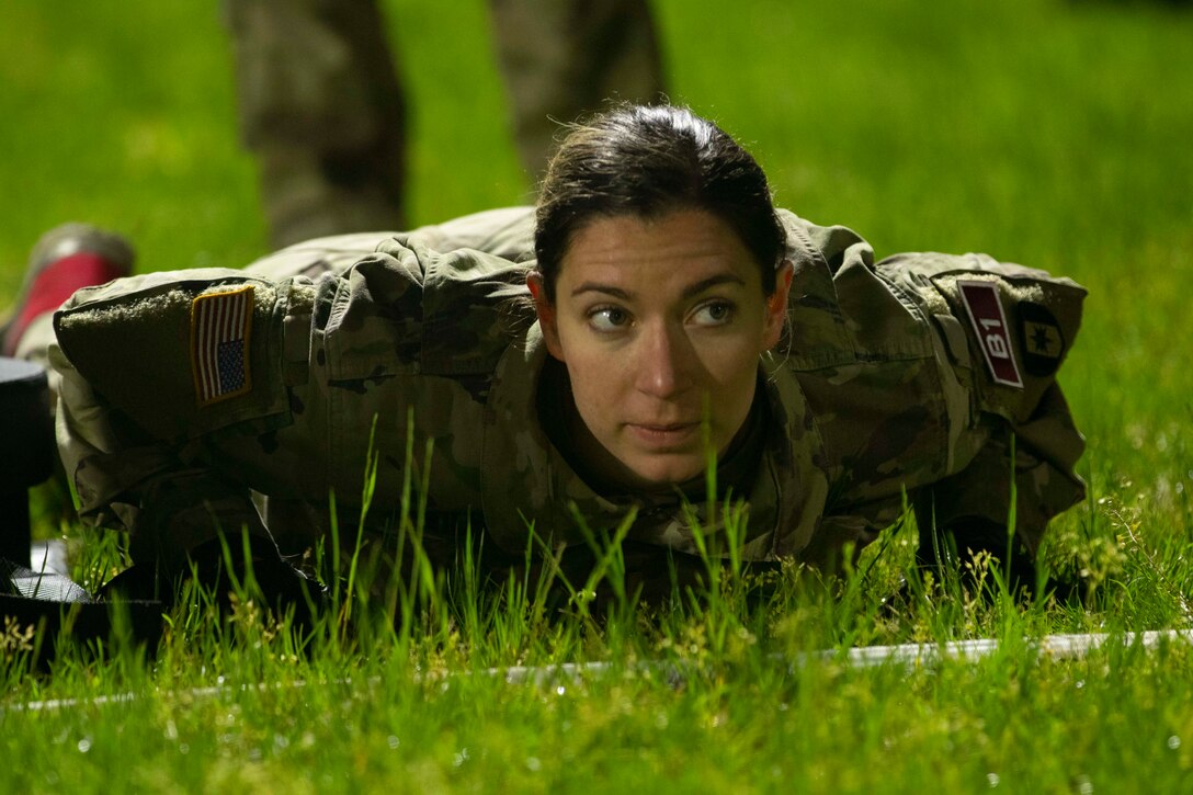 A woman waits intently while lying on her stomach with her fists at her sides in the grass.