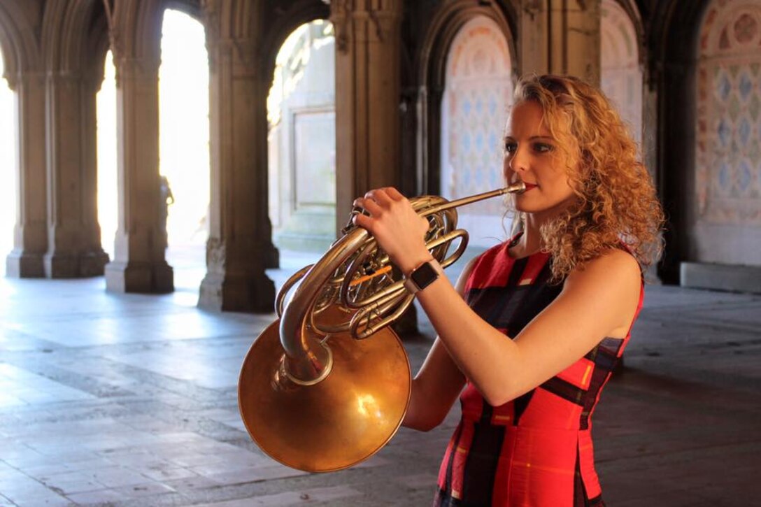 Woman in a red dress plays a French horn.
