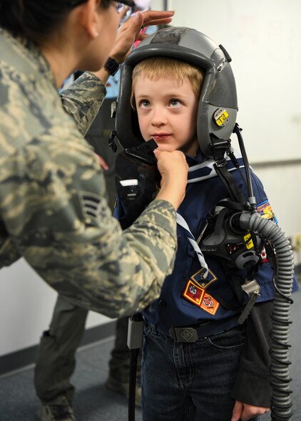 An Airman helps a Cub Scout put on a helmet