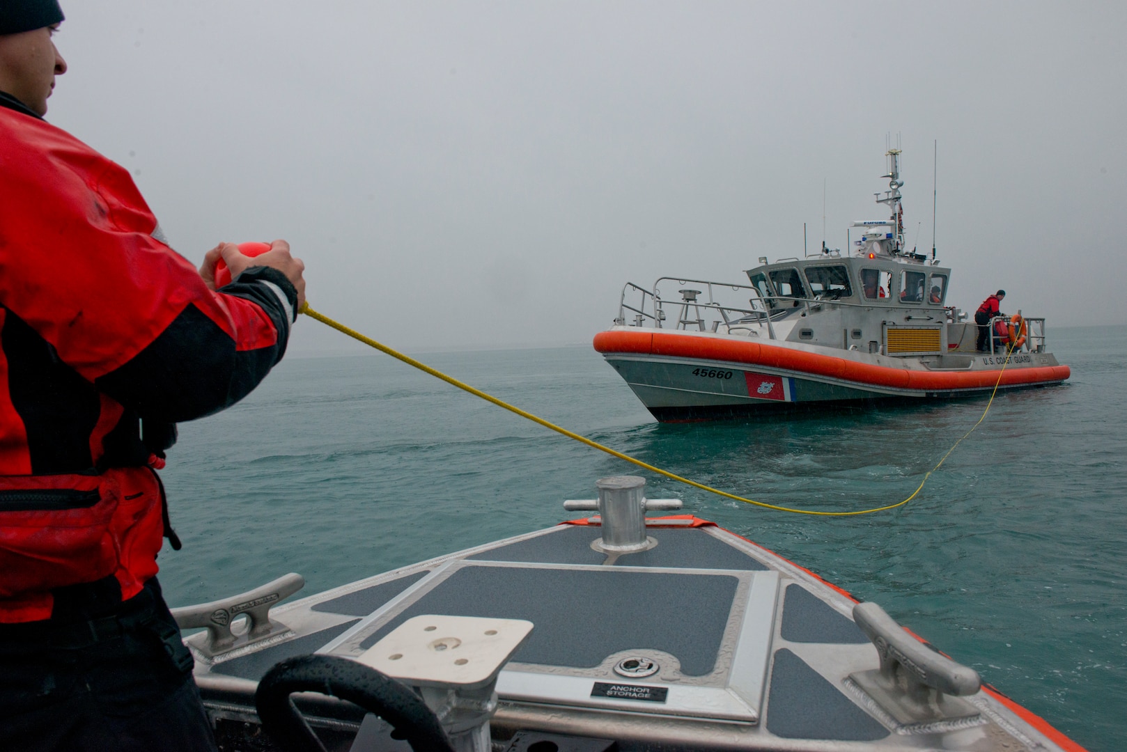 Coast Guard Petty Officer 3rd Class Alex Sheltra prepares to haul aboard a tow line after receiving a heaving line from a 45-foot Response Boat-Medium crew in the Port of Valdez, Alaska, Oct. 10, 2018. The  Station Valdez crews conducted training that included search patterns and vessel towing.