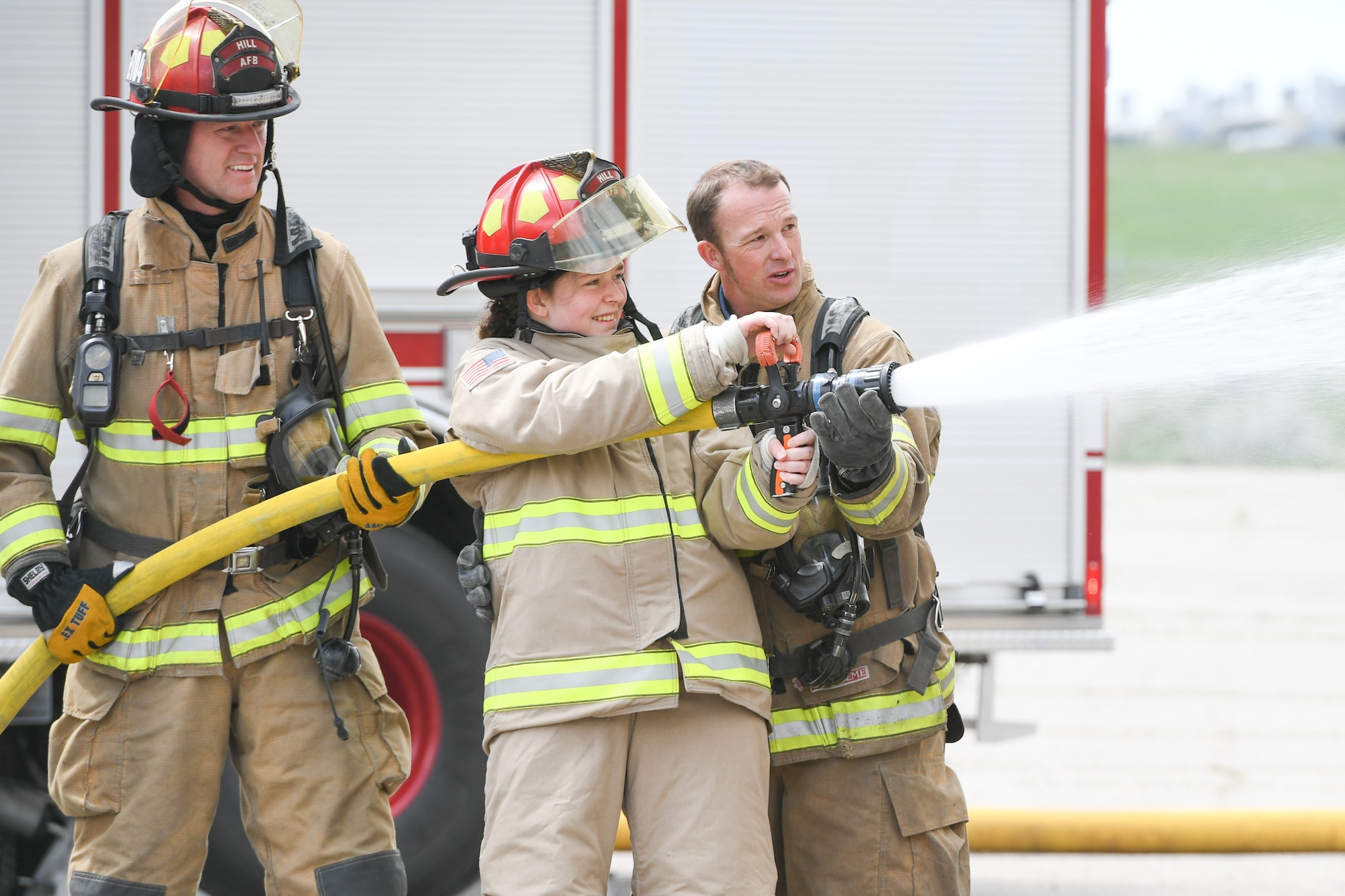 Michelle McConnell hoses a fire out with the guidance of Captain John Rice and Captain Daniel Payne, 775th Civil Engineering Squadron Firefighters, April 22, 2019 at Hill Air Force Base, Utah. Michelle was granted her wish to be Airman of the day by Make-A-Wish Utah and 75th Air Base Wing at Hill. (U.S. Air Force Photo by Cynthia Griggs)