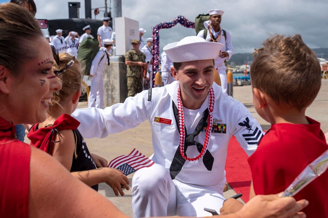 A sailor crouches down as his family comes in to hug him.