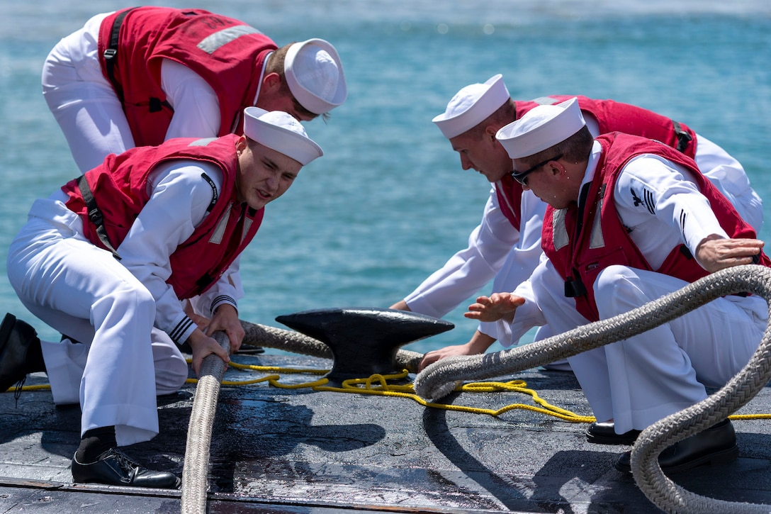 Four sailors pull a  rope around an anchor.