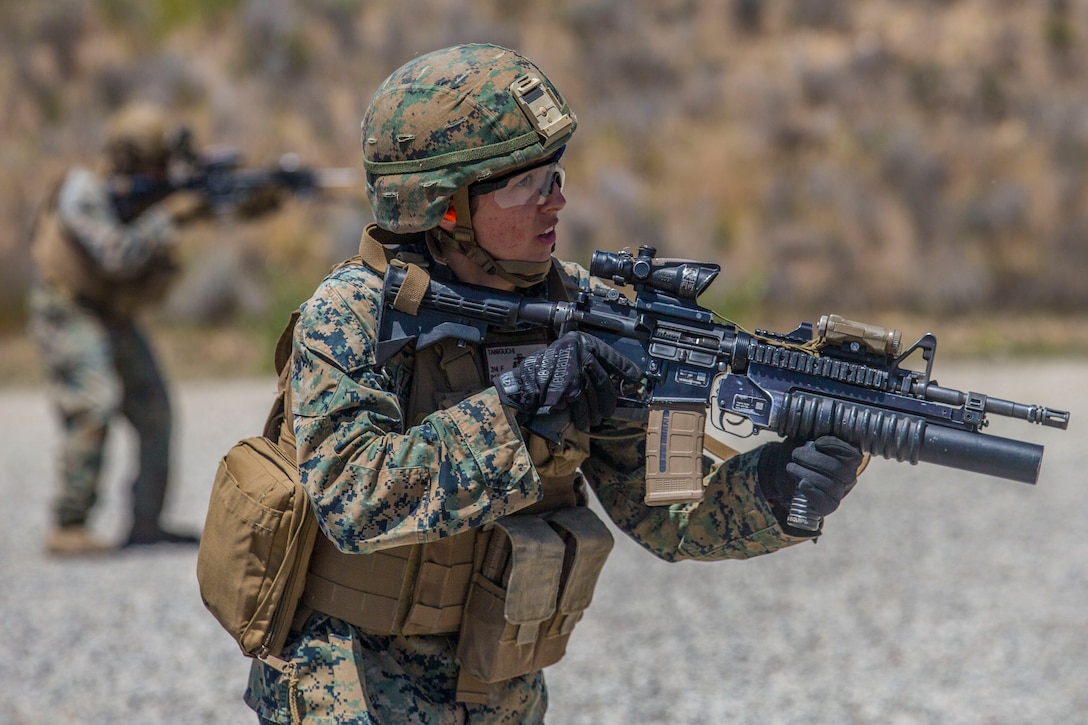 A Marine holds a weapon looking out in the distance.