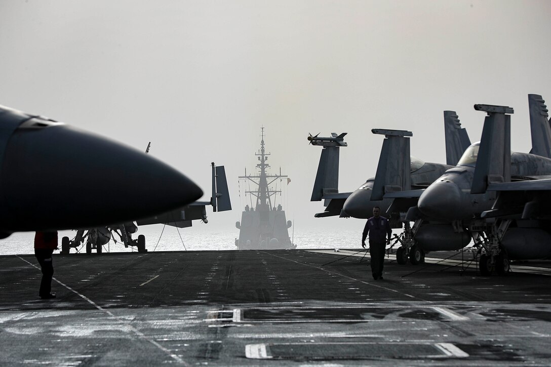 An aircraft carrier sails behind another ship.