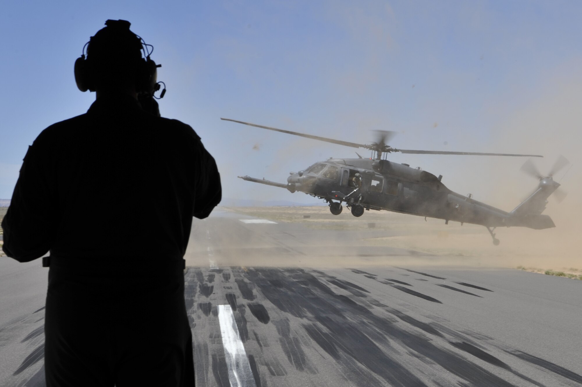 A loadmaster assigned to the 415th Special Operations Squadron, Kirtland Air Force Base, N.M., watches an HH-60G PAVE Hawk helicopter land during a training mission at Belen Alexander Airport, April 19, 2019, in Belen, N.M. The 415th SOS mission is to train special operations aircrew for the MC-130J Commando II and HC-130J Combat King II. (U.S. Air Force photo by Staff Sgt. Dylan Nuckolls/Released)