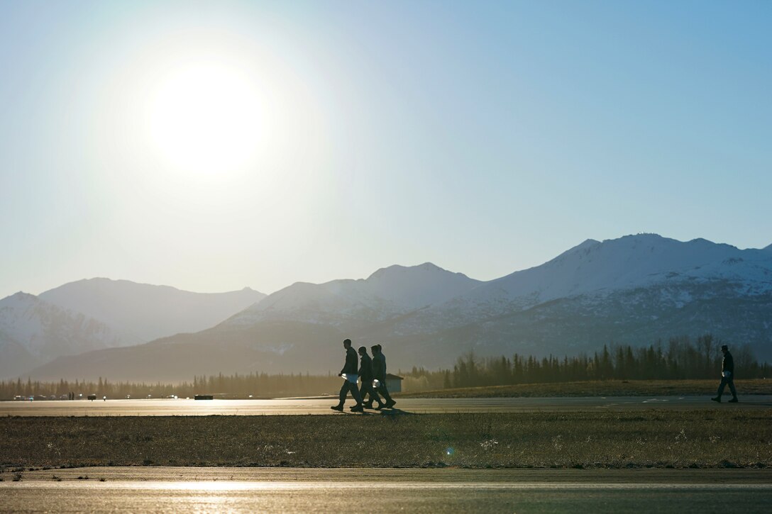 Three airman walk with the sun in the sky and mountains in the background.