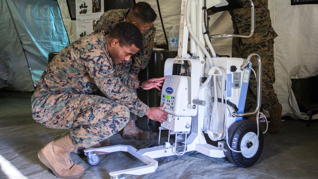 Two U.S. Navy corpsmen are crouched down to prepare the RadPRO X-ray machine