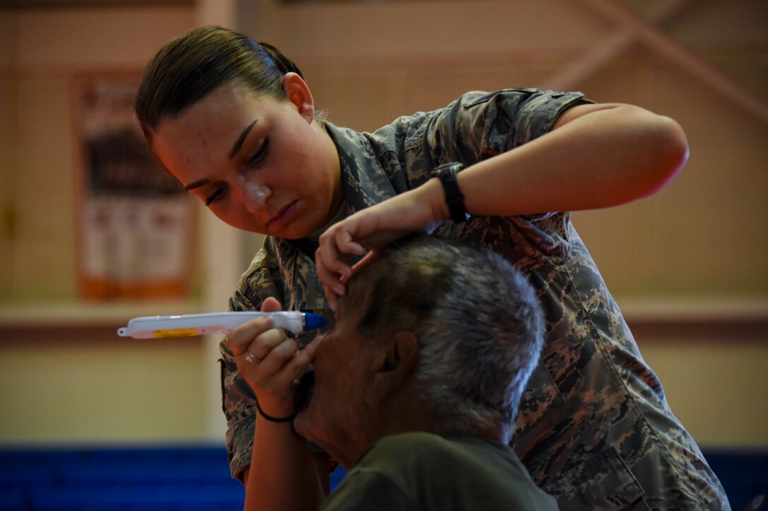 An airman uses a tool to look into a man's eye.