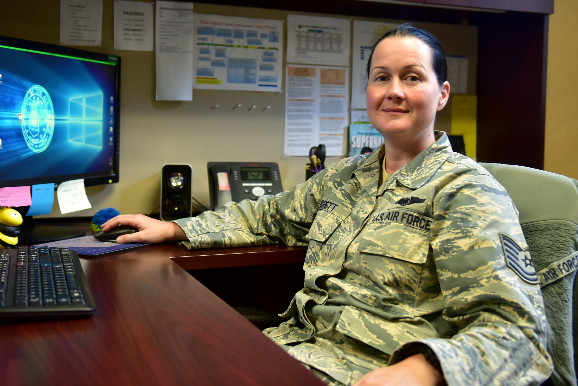 A woman wearing the Airman Battle Uniform sits at a desk.