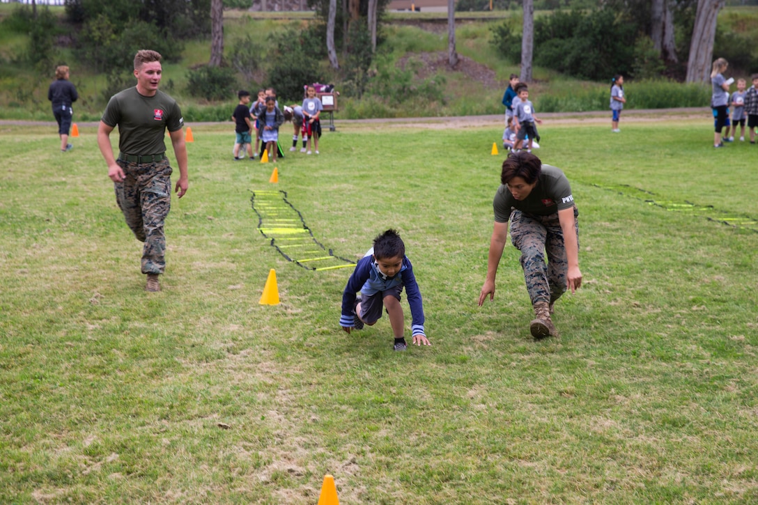 Lance Cpl. Adriana Royster (right) and Lance Cpl. Jacob Muller (Left), both with Marine Corps Air Station Miramar, assist a student complete the fitness challenge session at Miramar Ranch Elementary School in San Diego, April 26. The Marines came together for the Single Marine Program’s 5th annual “Days of Service” event, which involves Marines going to different locations off of the installation and doing their part in keeping the environment clean. (U.S. Marine Corps photo by Cpl. Preston Hightower)
