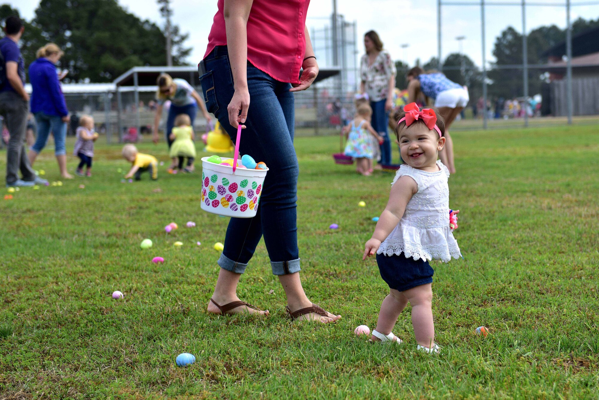 A young girl walks around a field full of Easter eggs.