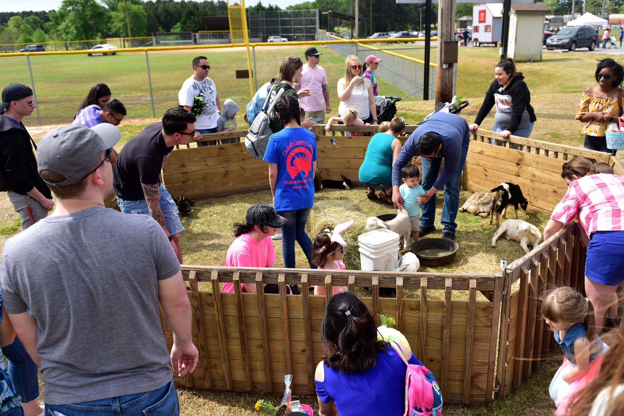 Many people are sitting in a pen petting numerous animals.