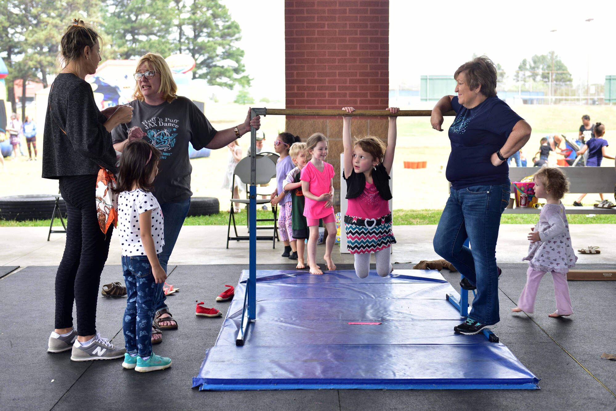 Young girls play on gymnastics equipment while being supervised by adults.