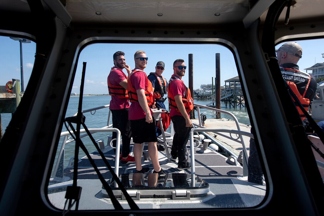 Four men look over their shoulders to listen to a Coast Guard member.