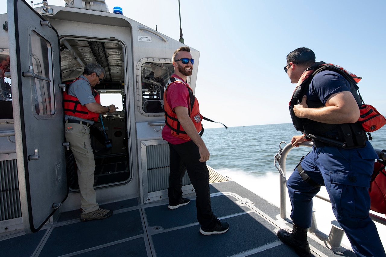 Two men in life vests stand near a door on a Coast Guard boat.