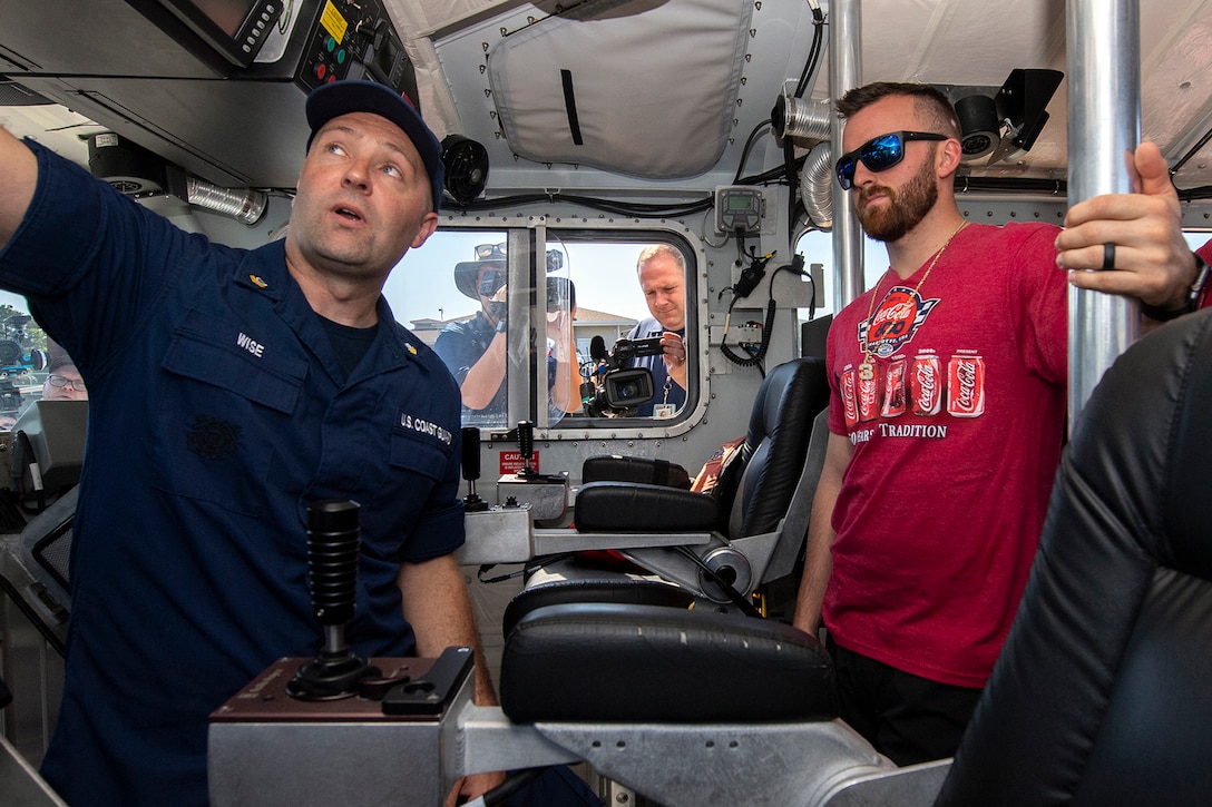 A man watches where a Coast Guard member in uniform points inside a boat.