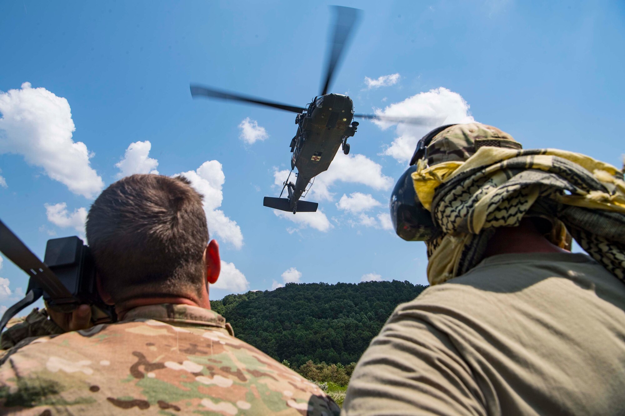 Two Airmen from the 130th Airlift Wing, McLaughlin Air National Guard Base, W.Va., look on as a U.S. Army UH-60 Blackhawk assigned to Company C., 2-104th General Support Aviation Battalion (MEDEVAC), Williamstown, W.Va., prepares to extract aircrew members from the field during combat survival training for Sentry Storm 19 held July 29, 2019, at the Hobet Mine site in Boone County, W.Va.