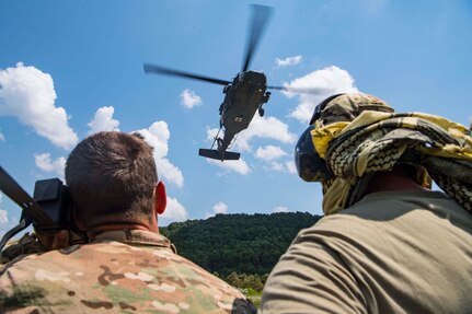 Two Airmen from the 130th Airlift Wing, McLaughlin Air National Guard Base, W.Va., look on as a U.S. Army UH-60 Blackhawk assigned to Company C., 2-104th General Support Aviation Battalion (MEDEVAC), Williamstown, W.Va., prepares to extract aircrew members from the field during combat survival training for Sentry Storm 19 held July 29, 2019, at the Hobet Mine site in Boone County, W.Va.