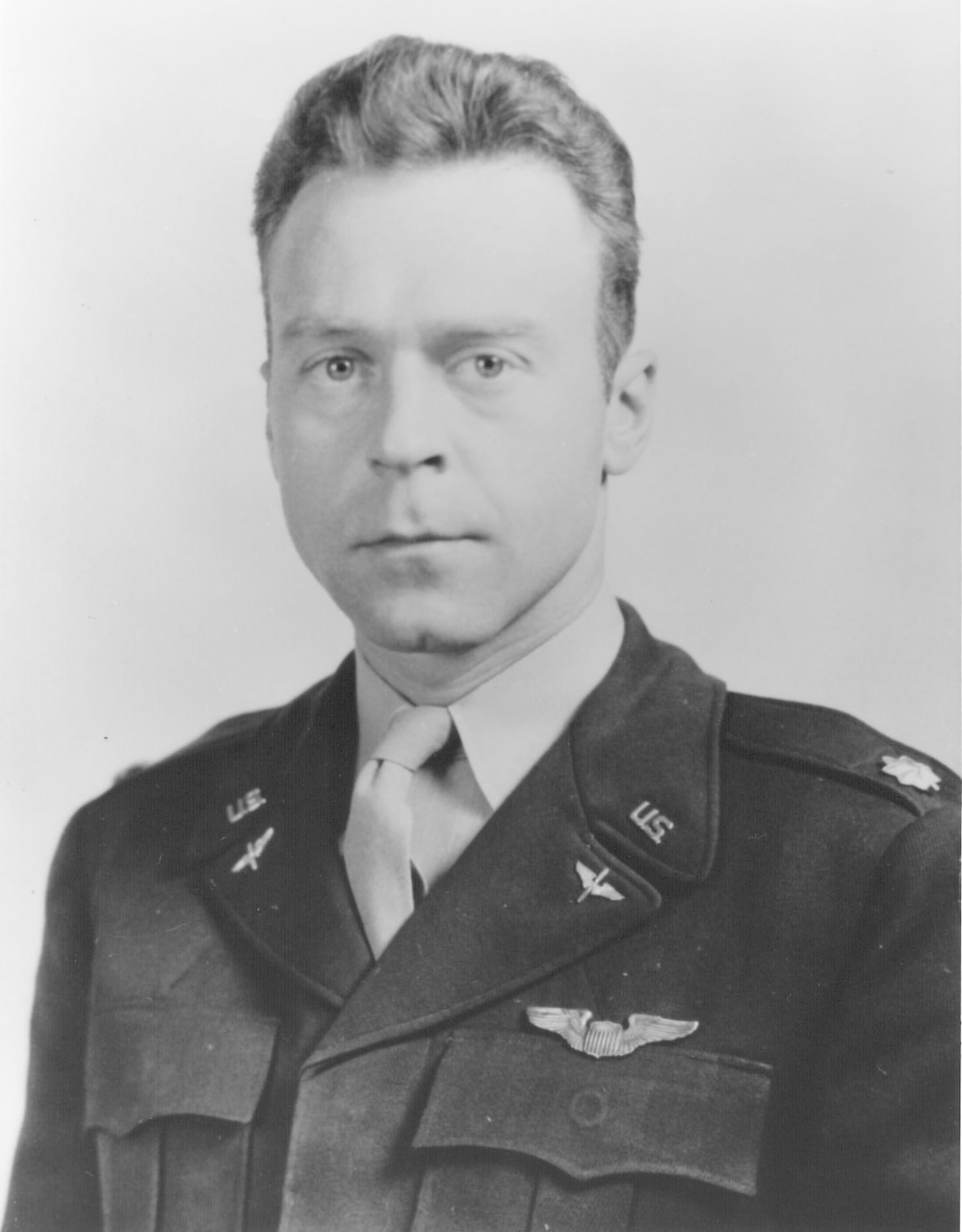 A man wearing an Air Force dress uniform looks at the camera. He has pilot’s wings on his lapel.