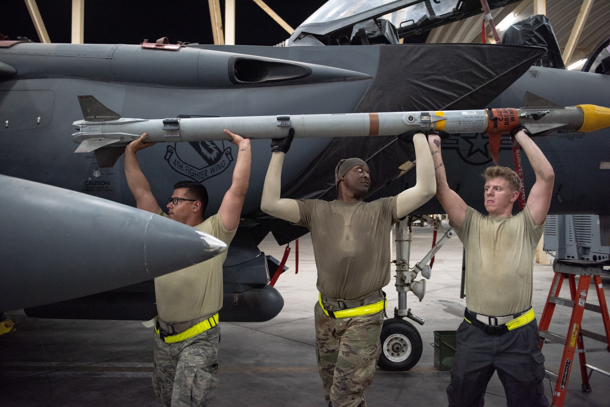 An F-15E Strike Eagle weapons load crew team lifts an AIM-9X Sidewinder missile to attach to a pylon July 15, 2019, at Al Dhafra Air Base, United Arab Emirates. The AIM-9X is an advanced infrared missile and the newest of the Sidewinder family of short-range air-to-air missiles carried on a wide range of fighter jets. (U.S. Air Force photo by Staff Sgt. Chris Thornbury)
