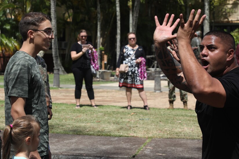 A teen and his little sister watch a man three feet away whose hands are up in the air.