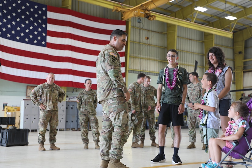 An Army colonel talks with a family in an aircraft hangar that has a large American flag draped in the background.