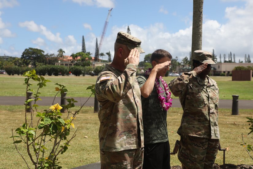 A teen wearing a Hawaiian lei and two soldiers salute an unseen object or person.