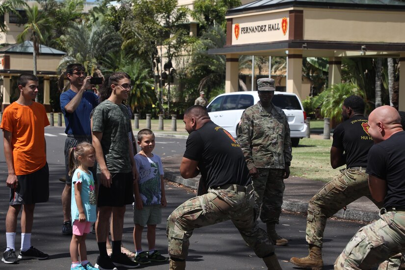 A family watches as several soldiers do a traditional Hawaiian warrior dance in front of them.