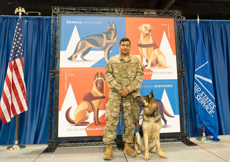 Military Working Dog Morty and Staff Sgt. Blake Radey, 55th Security Forces Squadron dog handler, pose for photograph next to the newly unveiled MWD stamp Aug. 1, 2019, at the Catholic Health Initiatives Health Center in Omaha, Nebraska. The stamp honors dogs that have served in the U.S. armed forces since the U.S. Army created the War Dog Program K-9 Corps and began training man’s best friend in March 1942. (U.S. Air Force photo by L. Cunningham)