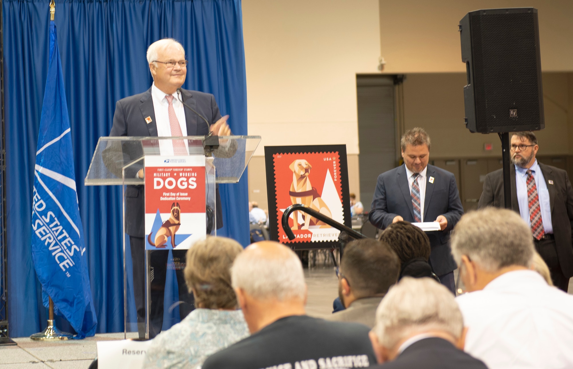 David C. Williams, United States Postal Service Board of Governors vice chairman, speaks at the unveiling of the Military Working Dog stamp Aug. 1, 2019, at the Catholic Health Initiatives Health Center in Omaha, Nebraska. The ceremony was held during the American Philatelic Society’s 133rd annual convention. (U.S. Air Force photo by L. Cunningham)