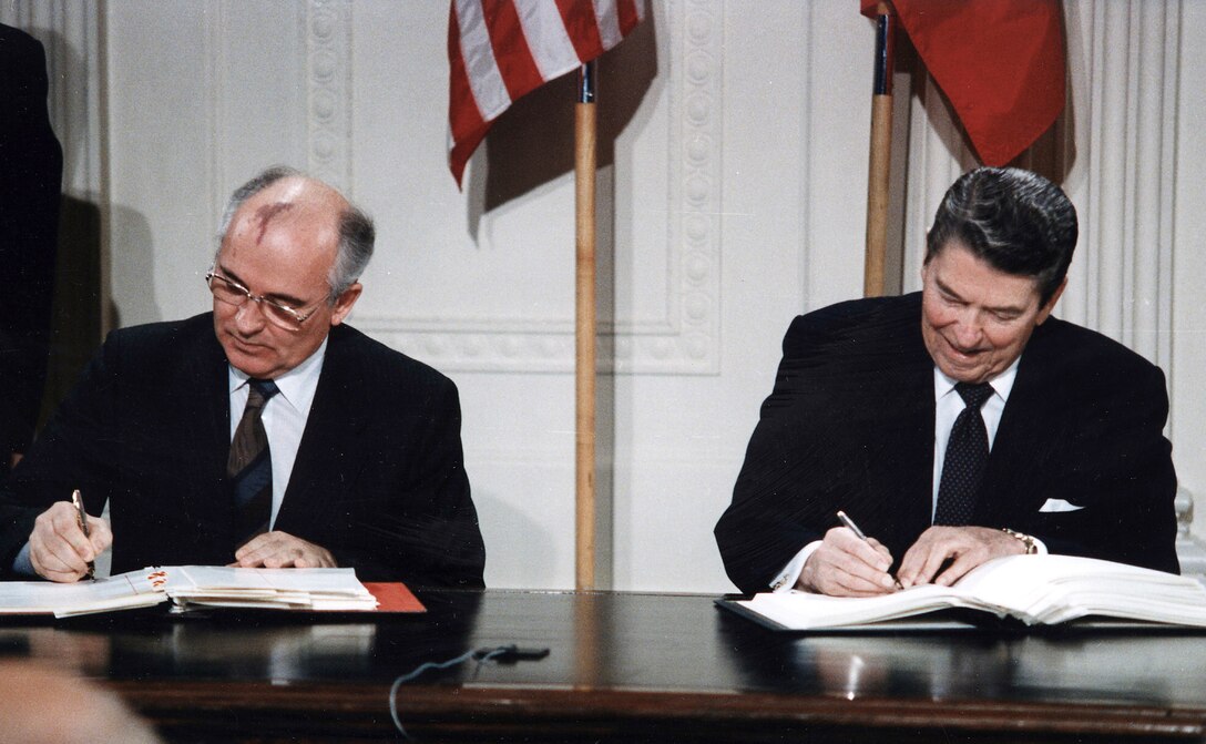 Two men sign documents at a desk.
