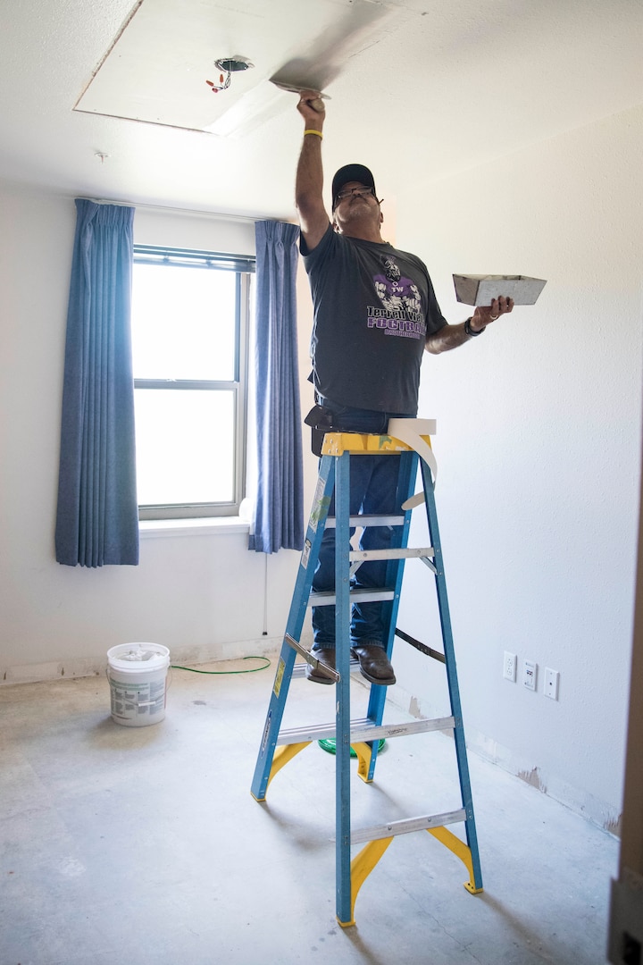 A Member of the 502nd Civil Engineering Group spreads joint compound on the ceiling of a dorm room impacted by mold August 1, 2019, at Joint Base San Antonio-Lackland, Texas. After an assessment, remediation steps include ensuring heating, ventilation and air conditions systems are properly working, as well as installing dehumidifiers, exhaust and ceiling fans. In order to reduce mold and humidity challenges, carpeting is being replaced with vinyl planking.