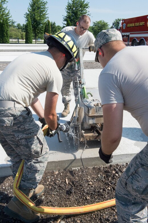Airmen from the Grissom Fire Department use water to keep the a concrete saw blade cool as Senior Airmen Jeffery Peters, 434th Civil Engineer Squadron pest management journeyman, saws relief cuts in a concrete pad at Grissom Air Reserve Base, Indiana Aug. 3, 2019. The training area will help accelerate readiness by providing realistic training sites. (U.S. Air Force photo/Tech. Sgt. Jami K. Lancette)