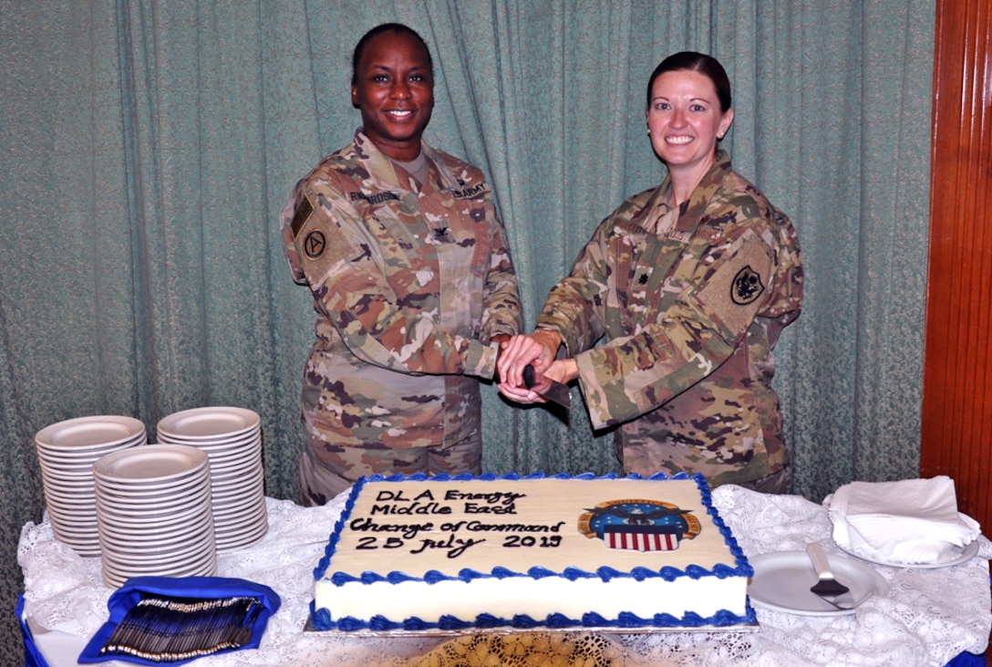 two women in uniform prepare to cut a cake