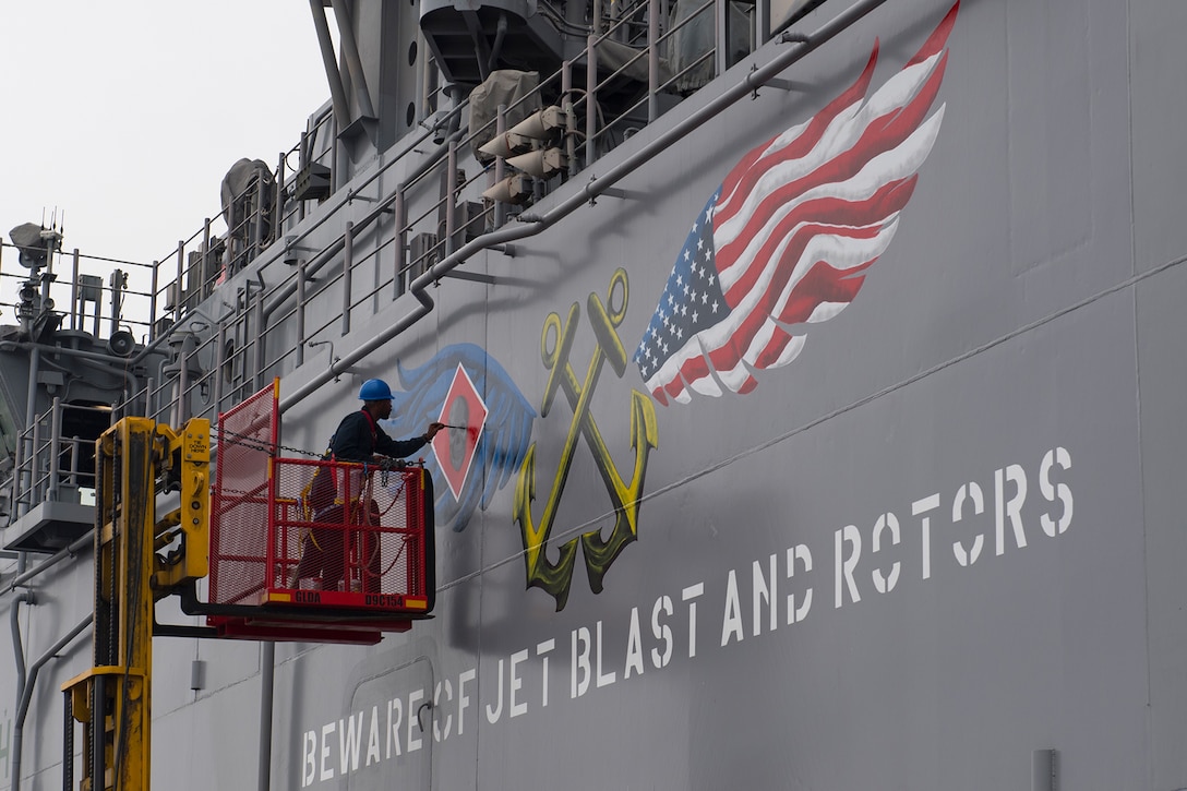 A sailor paints a logo on a ship.