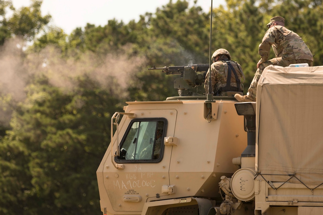 A soldier fires a gun while on top of a military vehicle.