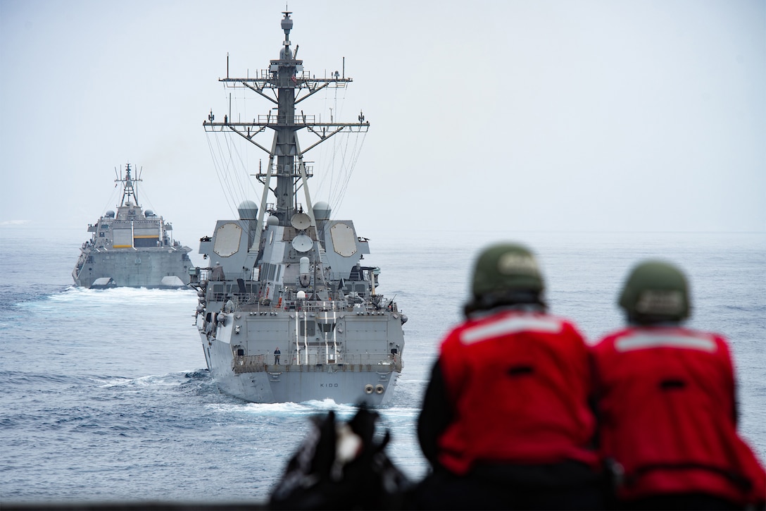 Two people watch ships sail in the ocean.