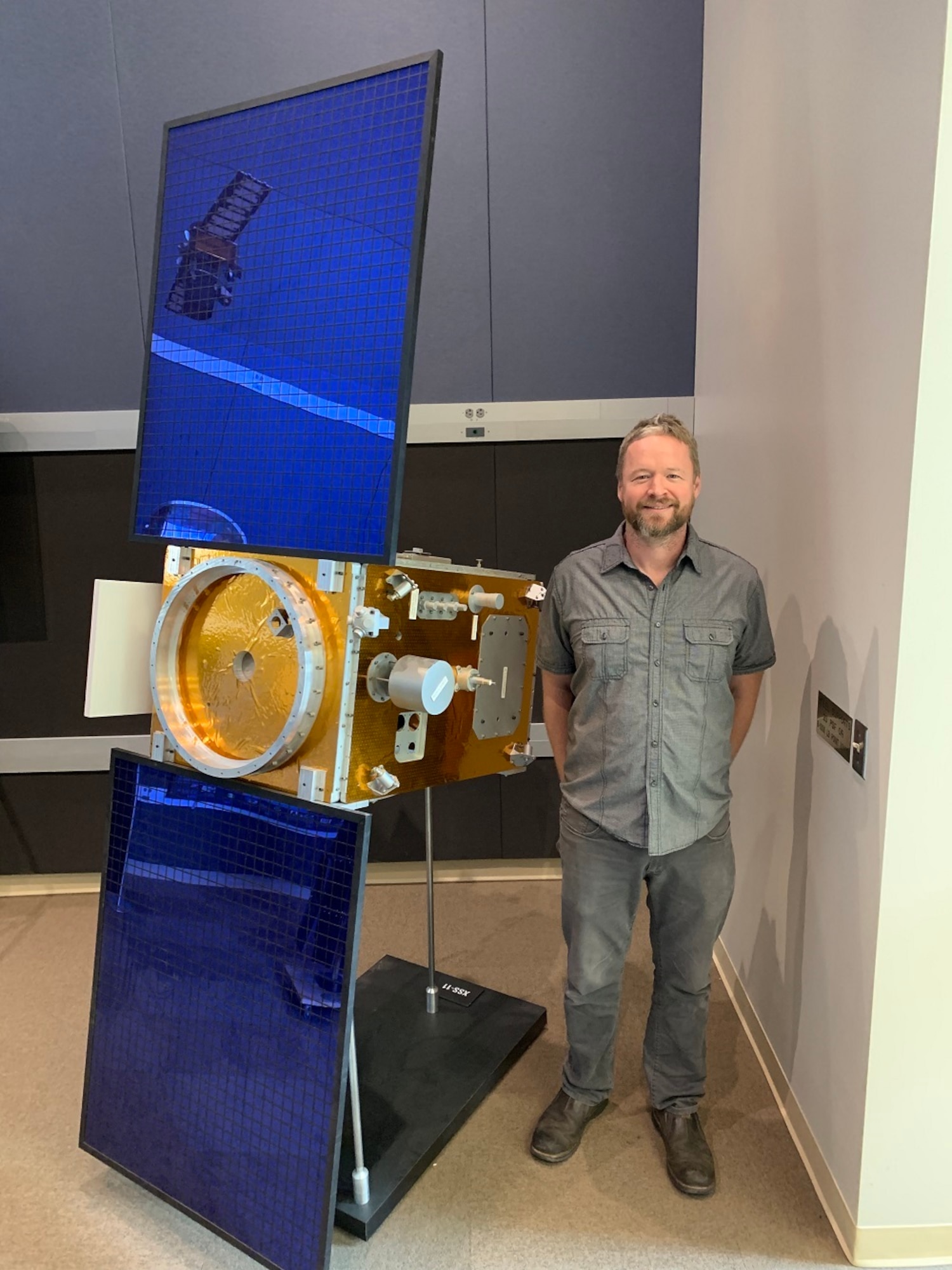Daniel Engelhart of Assurance Technology Corporation, displays a scale model of satellite XSS-11 which uses Kapton to manage the internal temperature of the satellite. Electron irradiation alters the optical and mechanical properties of the material, leading to non-ideal spacecraft thermal management. (Courtesy photo)