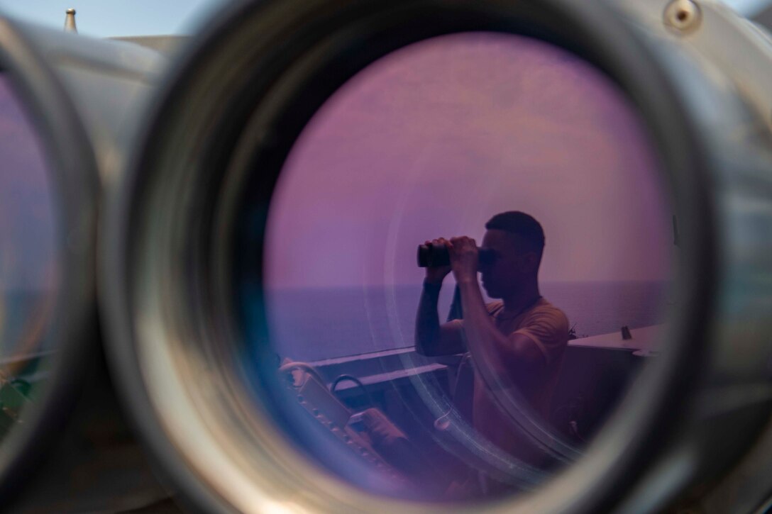 A sailor looks through binoculars.