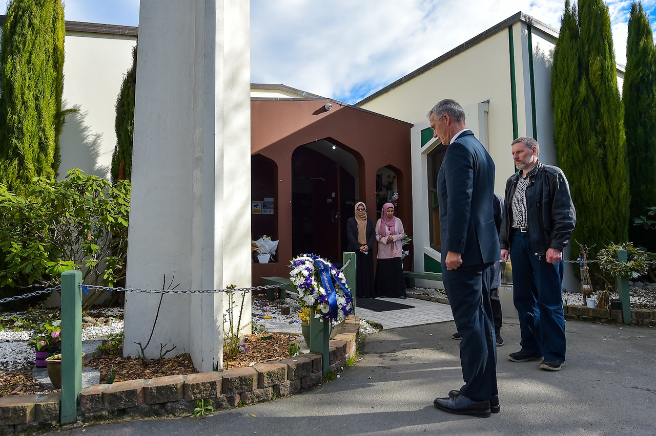 Man bows head in front of wreath.