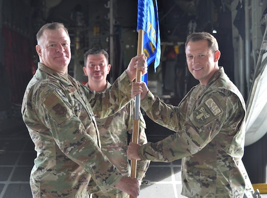 Two men holding a guidon and the first sergeant in the background standing by.