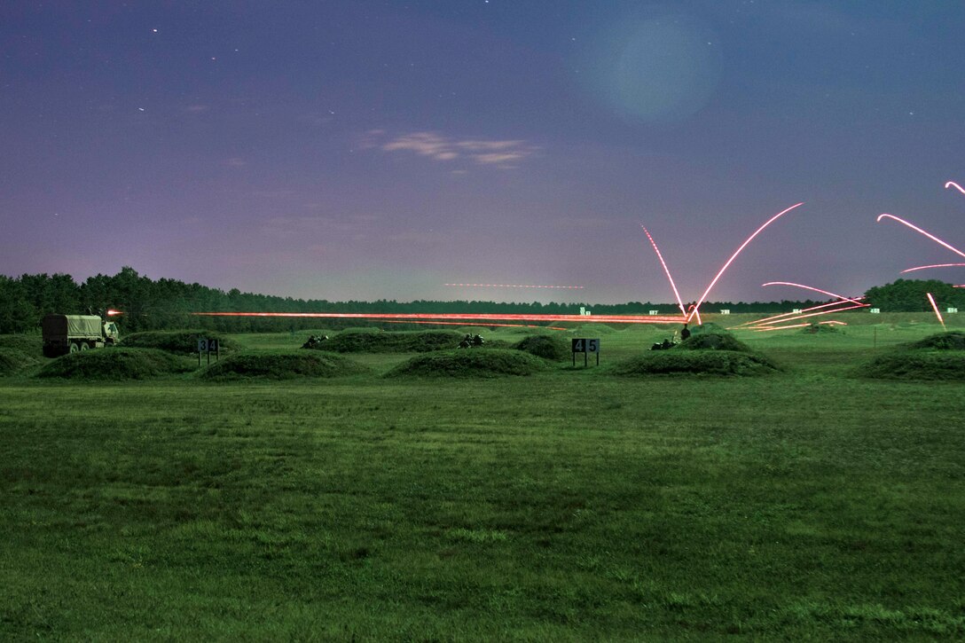 A truck fires a weapon at night, sending pink light beams across a grassy field.