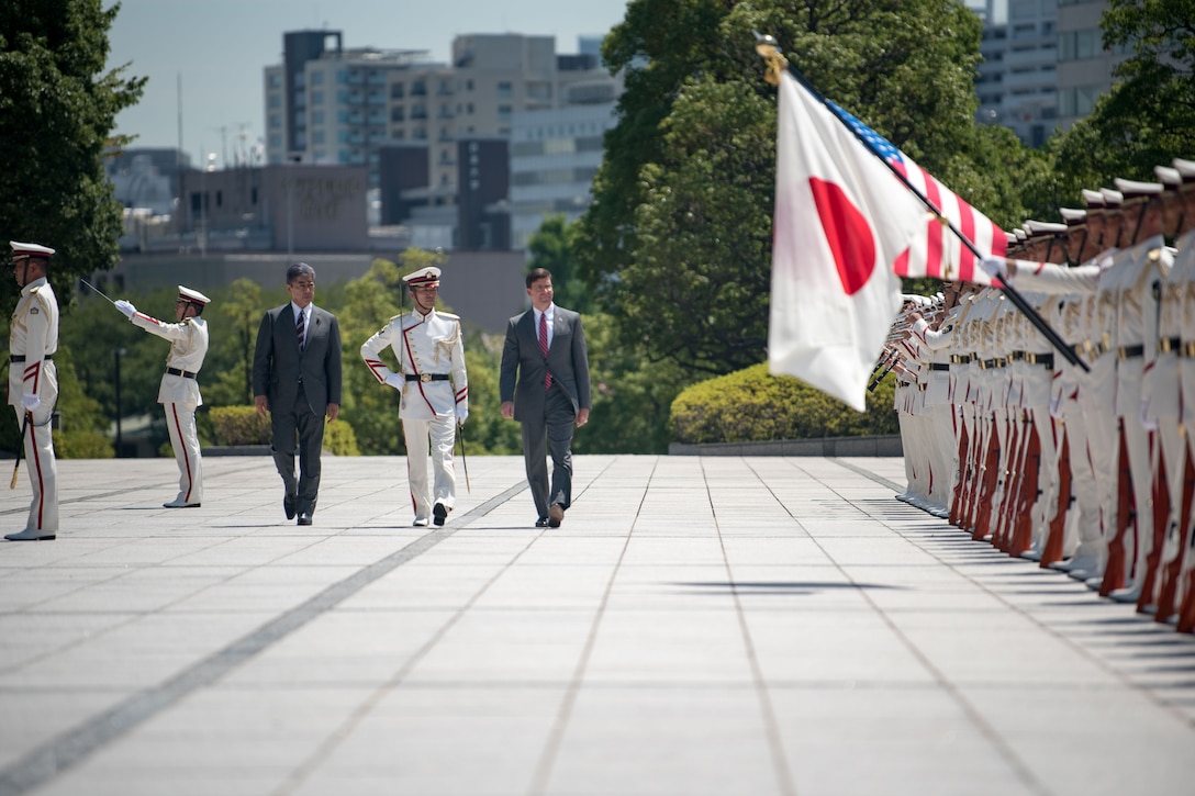 Three men walk together in front of troops.