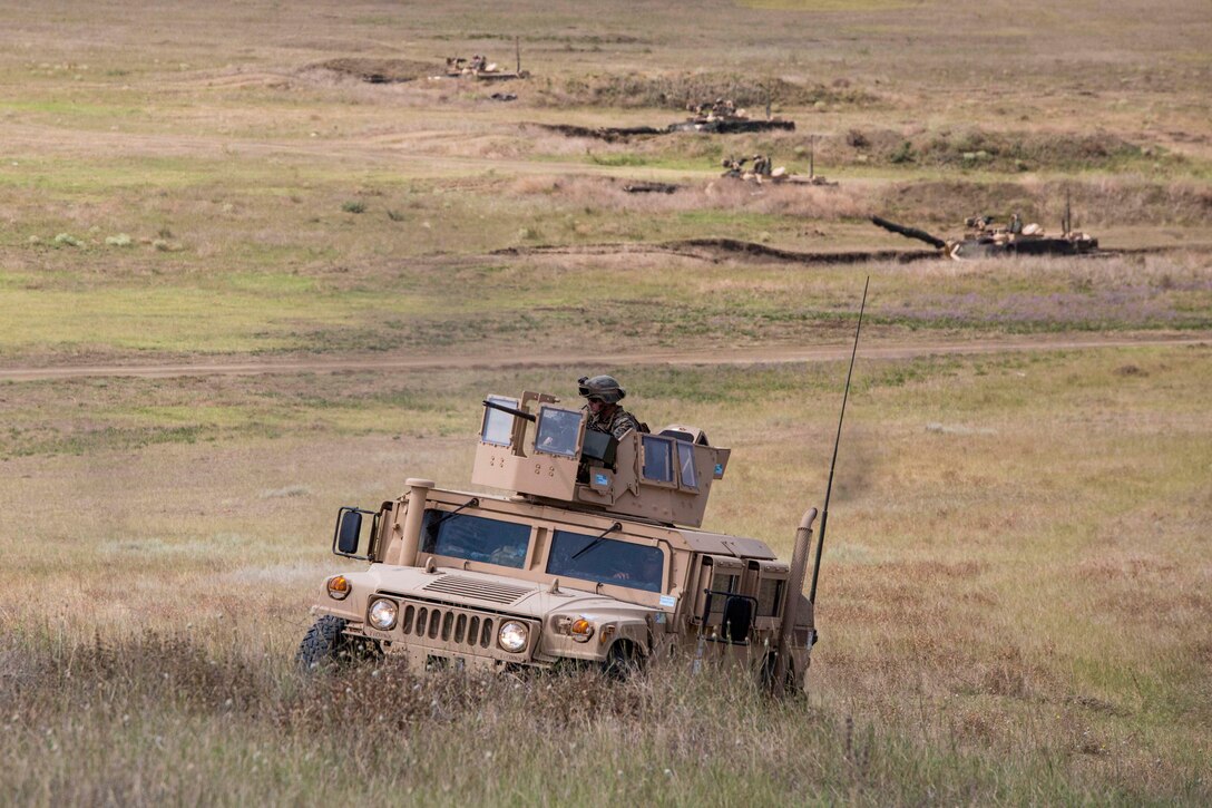 A Marine riding in a Humvee in desert terrain.