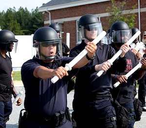 Officers in full gear train with batons.